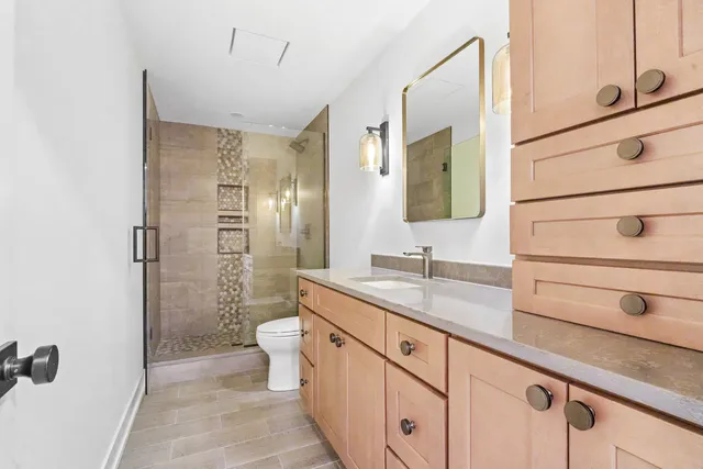 a bathroom with a granite countertop sink a toilet a mirror and shower