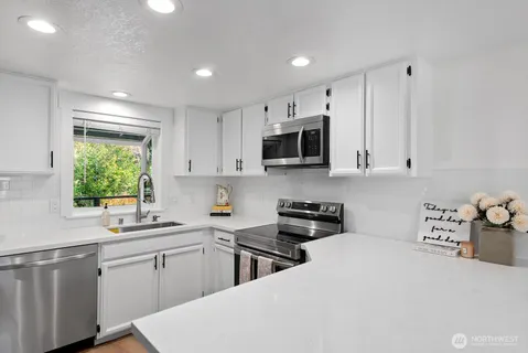 a kitchen with stainless steel appliances a sink a stove a microwave a refrigerator a window and cabinets