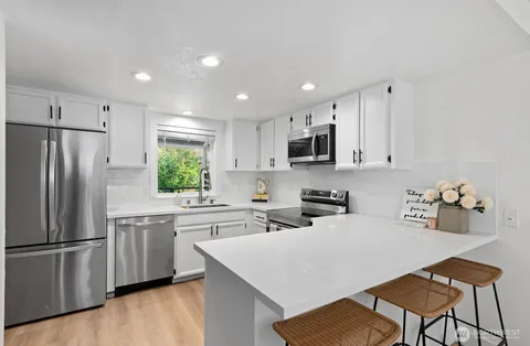 a kitchen with a refrigerator a stove a sink and white cabinets with wooden floor