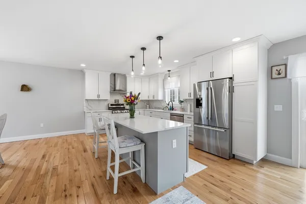 a large kitchen with stainless steel appliances kitchen island a stove a refrigerator a dining table and chairs with wooden floor