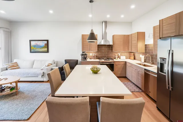 a living room with stainless steel appliances furniture a rug and a kitchen view