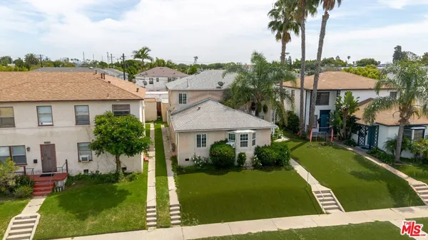 a view of a white house next to a yard with palm trees