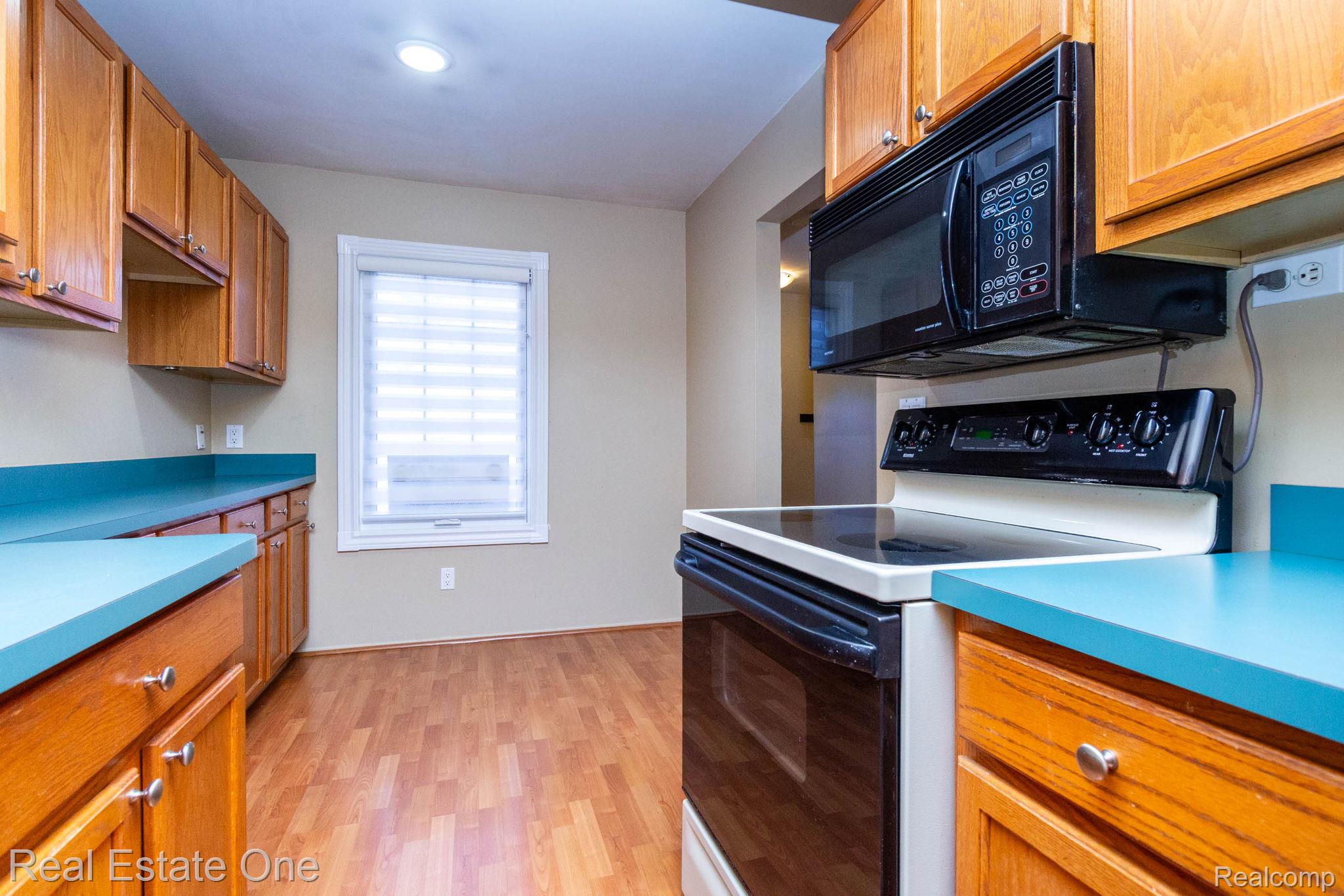 111 Manor Way Rochester, MI 48309 - Photo 14 of 36 Functional kitchen featuring wood-finish flooring, light wood cabinetry with silver hardware, teal countertops, and an integrated black microwave over a white electric range