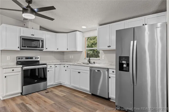 a kitchen with stainless steel appliances a refrigerator a sink dishwasher a stove and white countertops with wooden floor