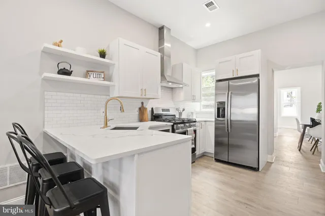 a kitchen with stainless steel appliances a refrigerator a sink a stove and white cabinets with wooden floor