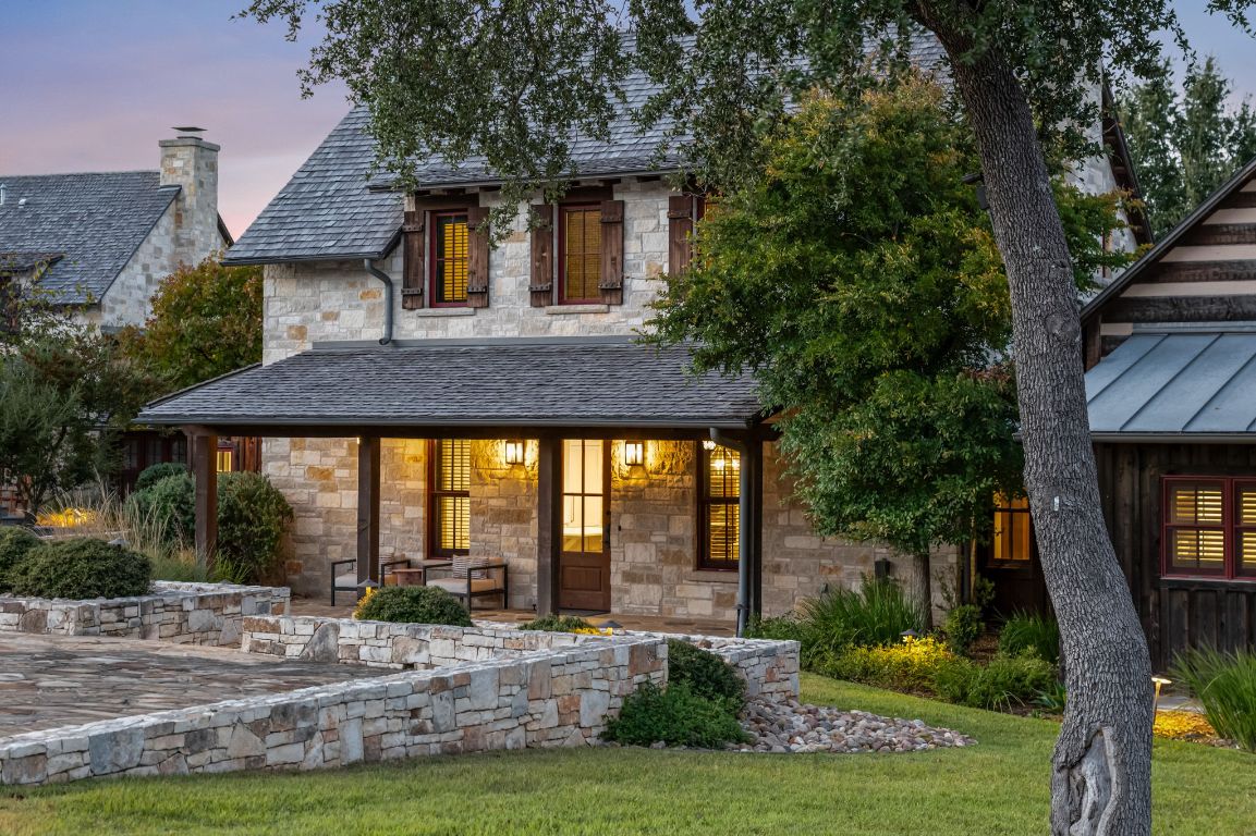 Twilight view of 65 Riviera Cove showcasing native stonework, inviting porch lighting, and the home’s classic Hill Country design.