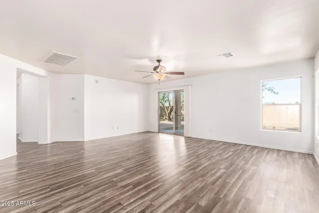 an empty room with wooden floor chandelier fan and windows