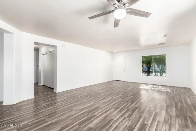 an empty room with wooden floor chandelier fan and windows