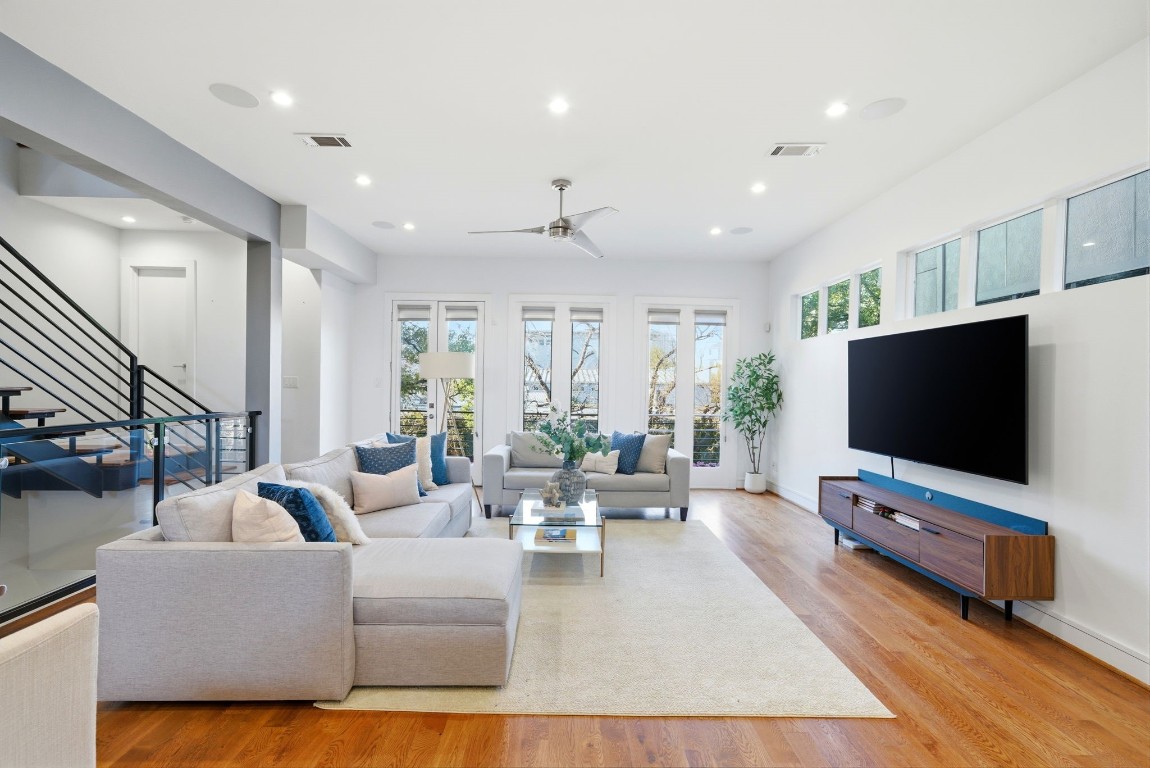 1405 Vermont Street, Unit A Houston, TX 77006 - Photo 11 of 46 High ceilings and polished hardwood floors anchor this light-filled living area, where an expansive layout offers seamless access to a private balcony through elegant French doors. Clerestory windows and tall glass panes invite abundant natural light, highlighting the contemporary designer finishes and sleek built-in media console. This sophisticated space at 1405 Vermont Street #A provides a luxury retreat for relaxation, perfectly positioned within the vibrant Bradford Mews community.