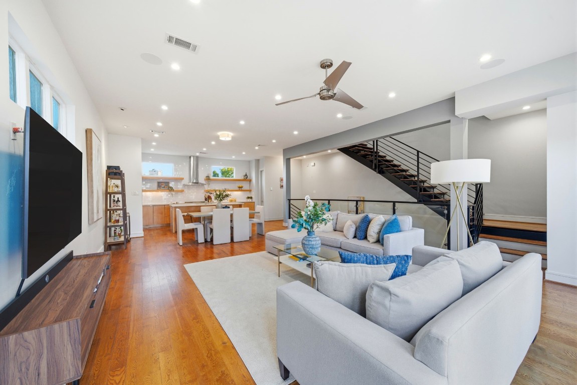 1405 Vermont Street, Unit A Houston, TX 77006 - Photo 13 of 46 Polished hardwood floors and soaring ceilings unify this expansive open layout, where a contemporary ceiling fan and recessed LED lighting enhance the airy atmosphere. The spacious living area flows seamlessly into the gourmet kitchen and dining zone, while a modern floating staircase with sleek black railings provides a striking architectural backdrop. Multiple window placements, including high clerestory accents, ensure the entire floor is bathed in abundant natural light.