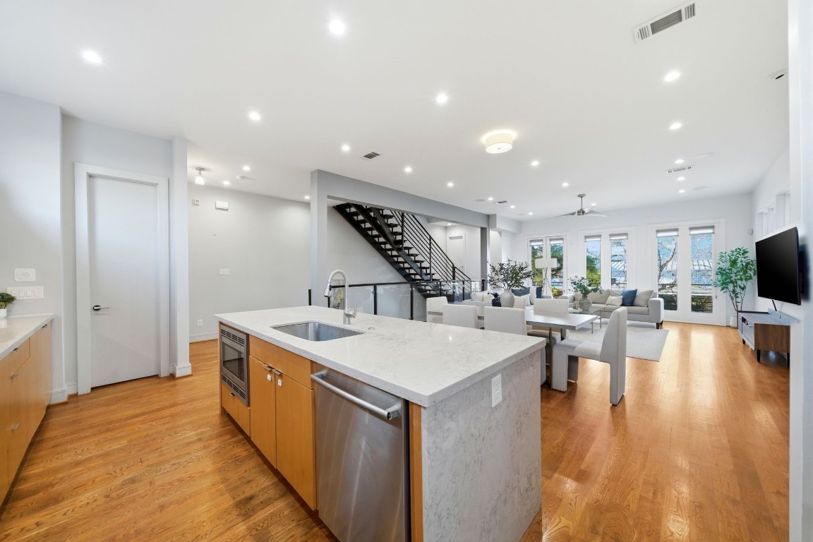 1405 Vermont Street, Unit A Houston, TX 77006 - Photo 17 of 46 Oversized quartz waterfall island serves as a sleek centerpiece for this expansive open layout, featuring a built-in microwave and professional-grade dishwasher. Hardwood floors flow seamlessly from the gourmet kitchen into the sun-drenched dining and living areas, where soaring ceilings and a modern floating staircase define the home's contemporary luxury. High clerestory windows and multiple sets of French doors bathe the entire second floor in abundant natural light.