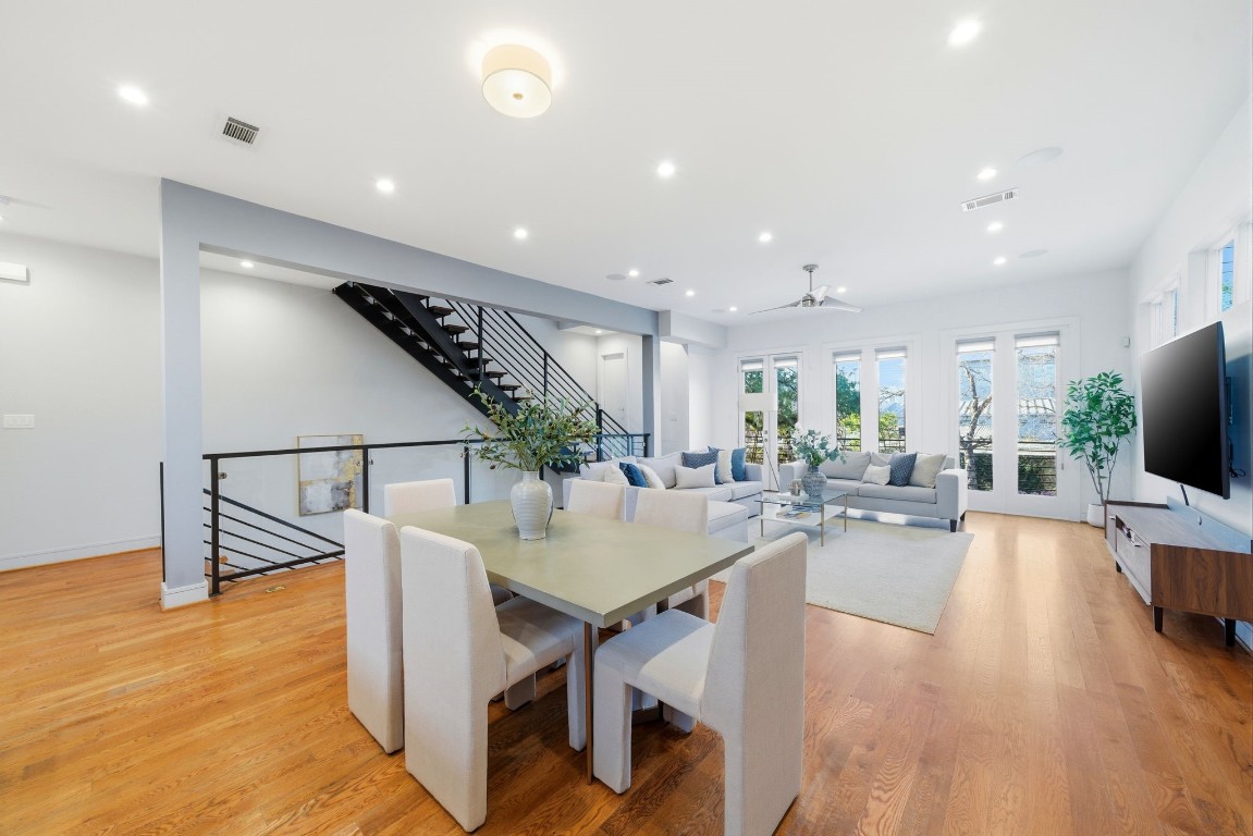 1405 Vermont Street, Unit A Houston, TX 77006 - Photo 20 of 46 Polished hardwoods and soaring ceilings unify this expansive living and dining area, where a modern floating staircase serves as a striking architectural backdrop. Abundant natural light pours through three sets of French doors that offer seamless access to the private balcony. Outdoor views and designer finishes enhance the open layout, creating a sophisticated atmosphere for hosting.