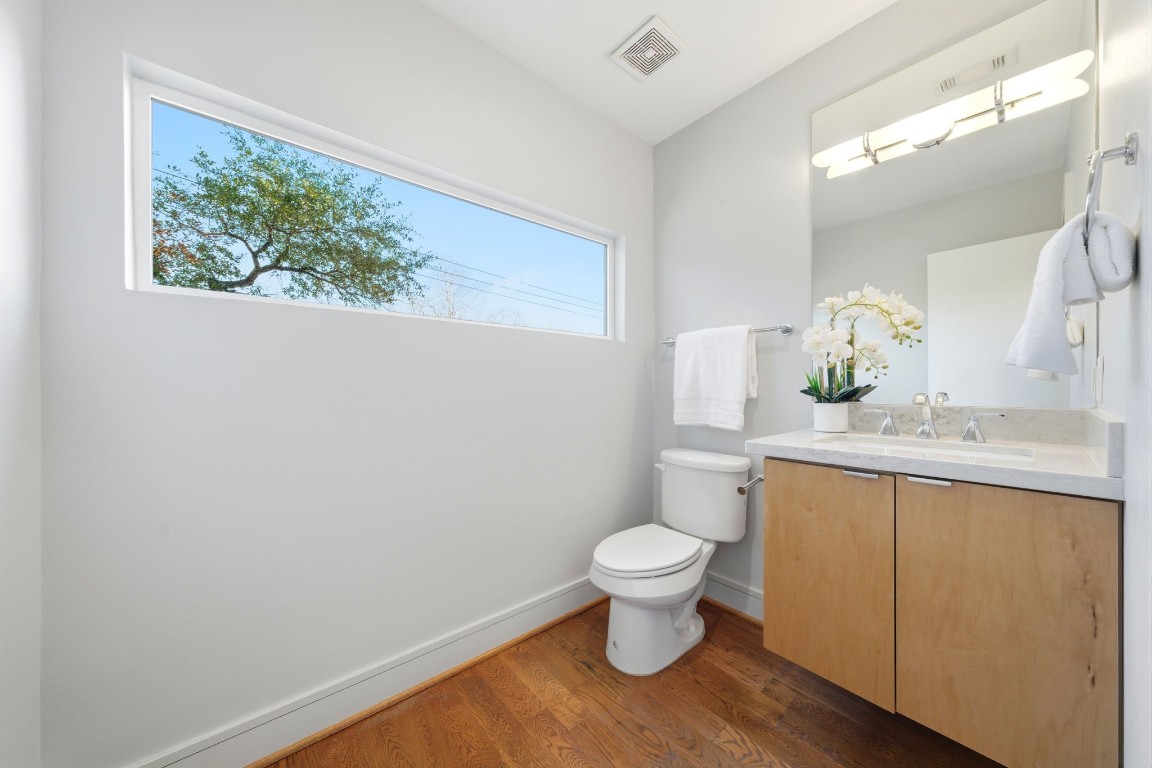 1405 Vermont Street, Unit A Houston, TX 77006 - Photo 22 of 46 Renovated powder bathroom combines contemporary style with functional luxury, featuring a floating wood vanity and sleek quartz countertops. A distinctive horizontal clerestory window provides a unique architectural element and peaceful treetop views, while the polished hardwood floors maintain a sophisticated continuity throughout the home.
