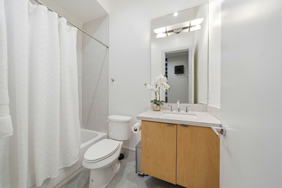 1405 Vermont Street, Unit A Houston, TX 77006 - Photo 24 of 46 Renovated secondary bathroom features a floating wood vanity paired with a sleek quartz countertop and a contemporary rectangular sink. A classic tub-and-shower combination is accented by designer tile and a clean white curtain, while a large vertical mirror enhances the space's airy atmosphere.