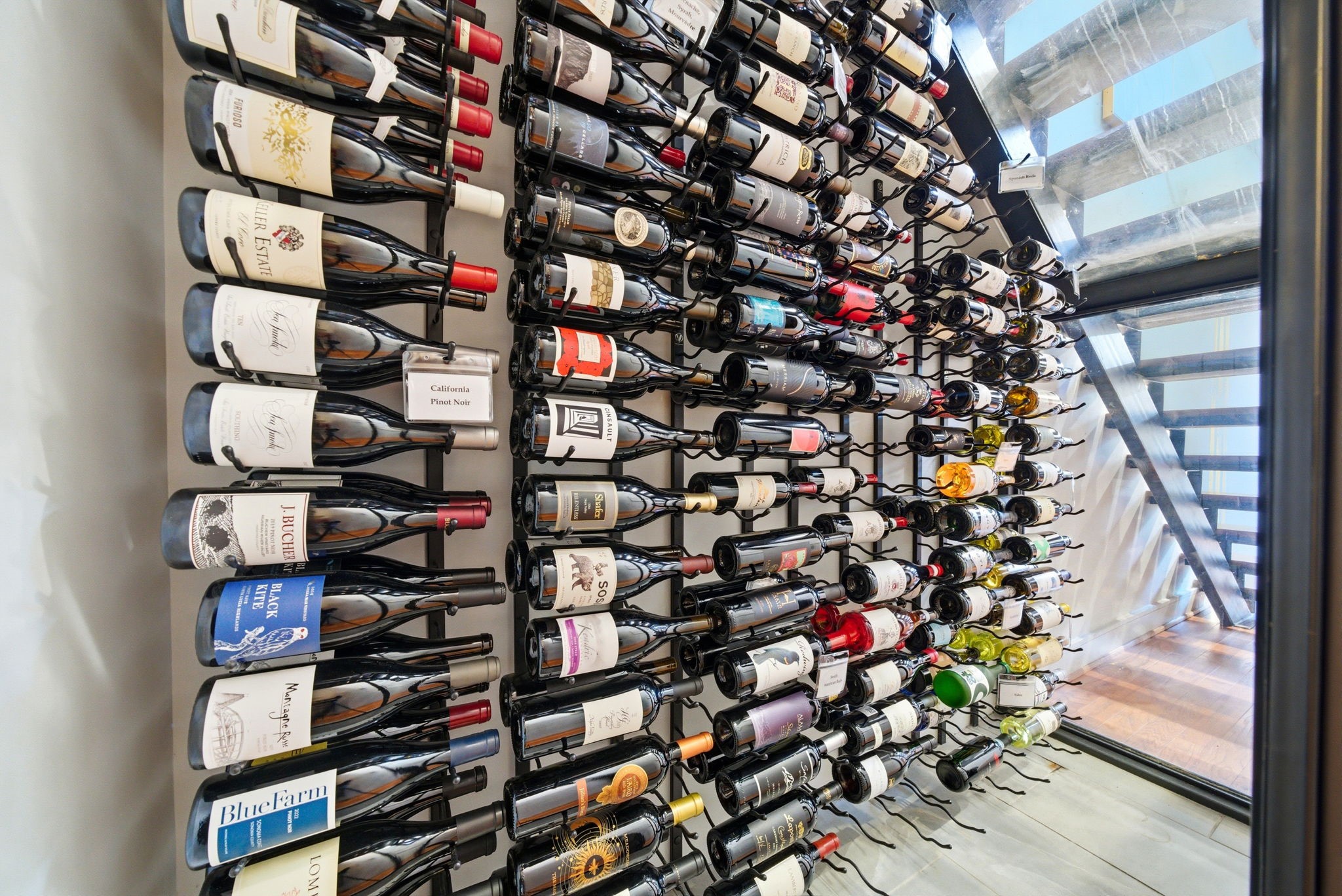 1405 Vermont Street, Unit A Houston, TX 77006 - Photo 26 of 46 High-capacity wall-mounted display showcases an extensive collection within this climate-controlled, glass-enclosed cellar. Rows of horizontal racks offer a sophisticated presentation beneath the modern floating staircase, blending luxury utility with contemporary design. Individual labeling and precision spacing ensure this high-capacity storage is both functional and a striking architectural focal point.