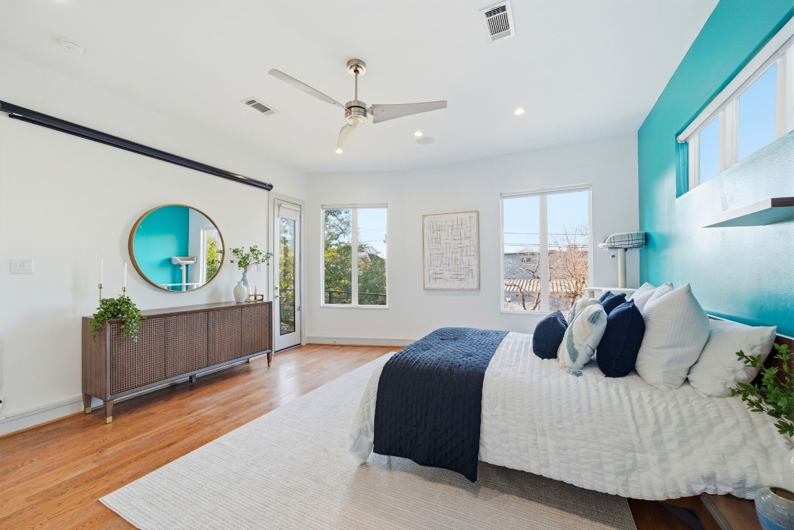 1405 Vermont Street, Unit A Houston, TX 77006 - Photo 28 of 46 A vibrant teal feature accent wall anchors this expansive primary retreat, where high ceilings and polished hardwoods create an airy, luxury atmosphere. Wide windows and a glass-paneled door offer abundant natural light and seamless access to a private balcony for peaceful morning coffee. Designer finishes, including a sleek three-blade ceiling fan and recessed LED lighting, complement the spacious layout that easily accommodates a king-sized suite and additional seating.