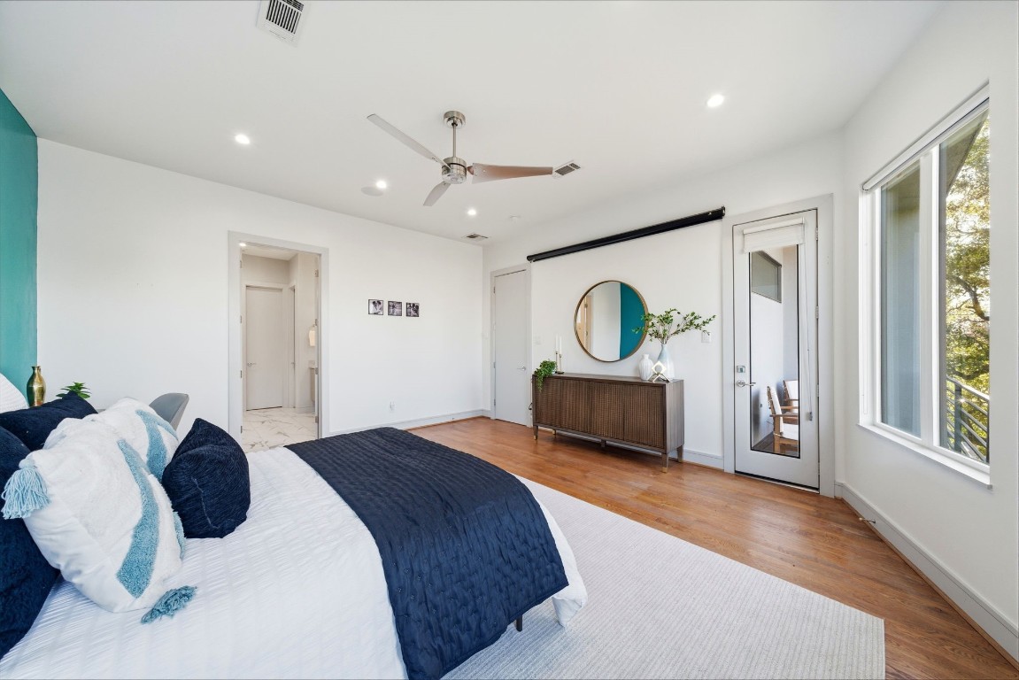 1405 Vermont Street, Unit A Houston, TX 77006 - Photo 29 of 46 Expansive primary bedroom features polished hardwood floors and high ceilings, offering a sophisticated retreat with a vibrant teal feature accent wall. A glass-paneled door leads to a private balcony, while the spacious layout provides ample room for a large dresser and a king-sized suite. Abundant natural light from wide windows highlights the designer finishes and seamless flow into the ensuite bath and walk-in closet.