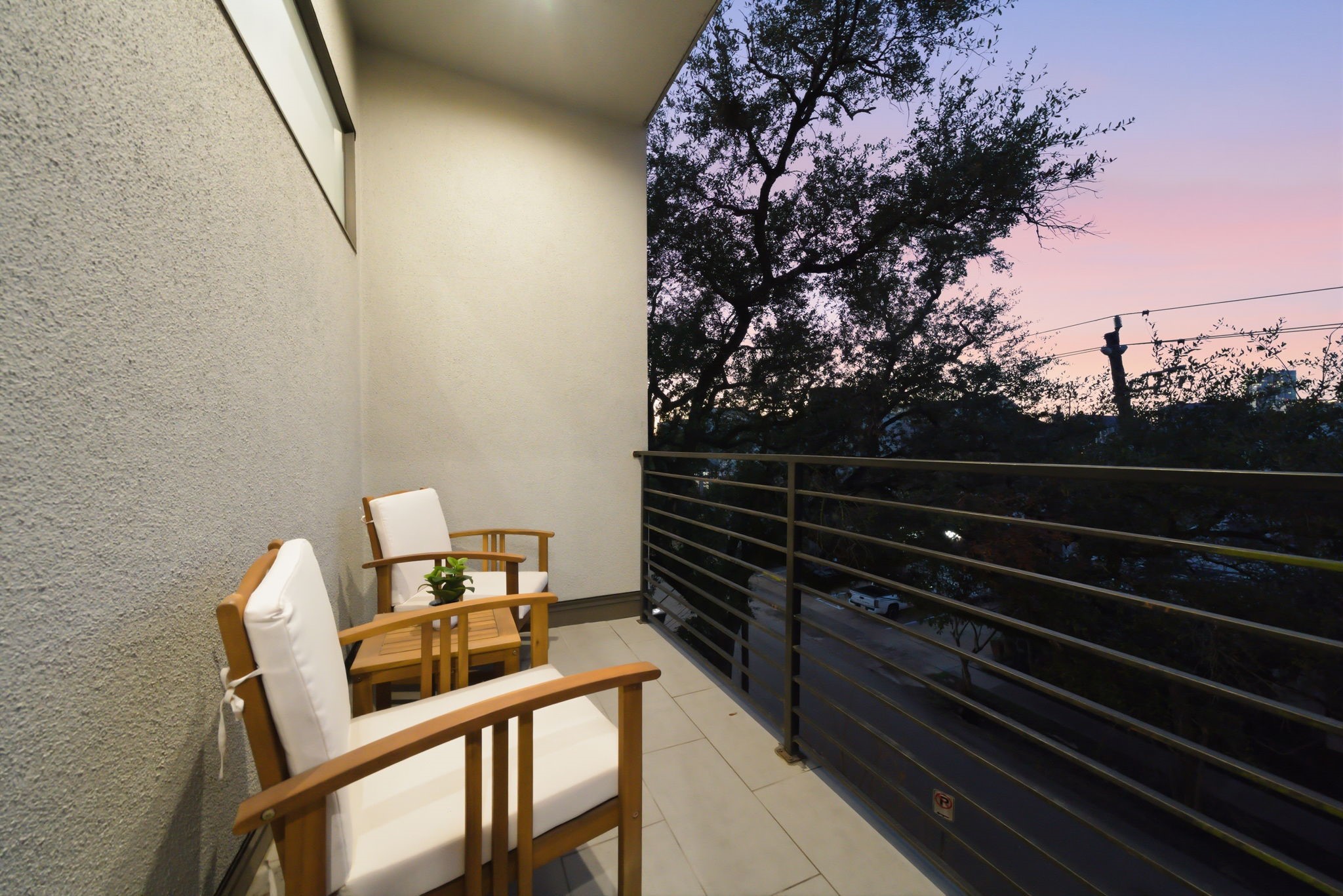 1405 Vermont Street, Unit A Houston, TX 77006 - Photo 32 of 46 Accessed through the primary suite, this private balcony offers a secluded seating area for enjoying city views and quiet mornings. Sleek metal railings and low-maintenance tile flooring create a sophisticated contemporary retreat. Large trees provide a natural canopy, blending the home's luxury stucco exterior with the peaceful Inner Loop streetscape.