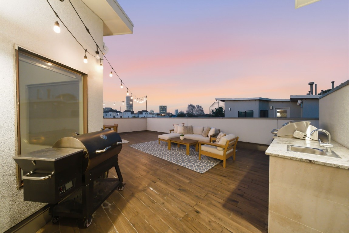 1405 Vermont Street, Unit A Houston, TX 77006 - Photo 38 of 46 Gourmet summer kitchen with a gas grill, sink, and granite countertops anchors this expansive rooftop deck. String lights hang above the low-maintenance flooring, illuminating the lounge area and dining space. This private Bradford Mews retreat offers a sophisticated setting for hosting guests while enjoying the open-sky views of the Houston skyline.