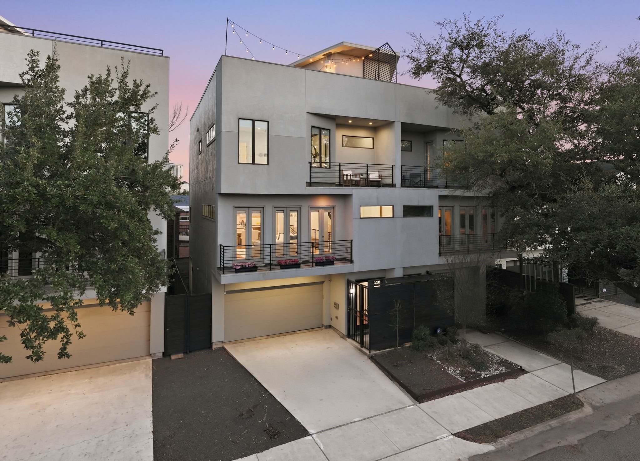 1405 Vermont Street, Unit A Houston, TX 77006 - Photo 41 of 46 Modern stucco and siding define the sophisticated facade of 1405 Vermont Street #A, a luxury three-story Bradford Mews residence. This contemporary home features a private driveway leading to a 2-car garage, while multiple glass-railed balconies and a rooftop deck with string lights showcase premier Inner Loop living. Low-maintenance landscaping and lush trees frame the entrance of this light-filled sanctuary, perfectly positioned for a quick commute to Downtown and the Medical Center.