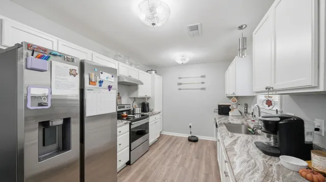 a kitchen with stainless steel appliances a refrigerator a sink dishwasher a oven with white cabinets and wooden floor