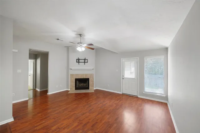 an empty room with wooden floor fireplace and windows