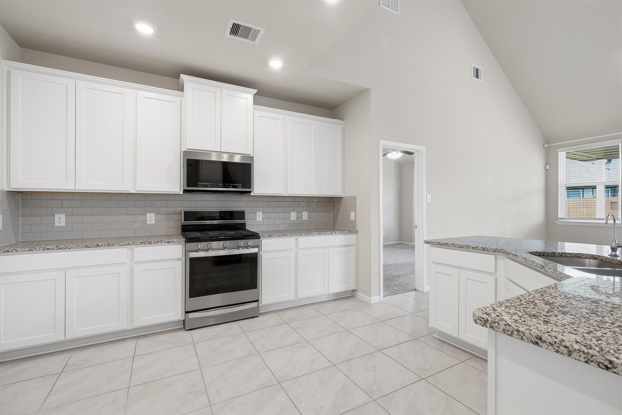 2413 Olancha Drive Rosharon, TX 77583 - Photo 9 of 41 A modern, open-concept kitchen with white cabinetry, granite countertops, and stainless steel appliances. It opens to a tiled living area, providing a spacious feel.