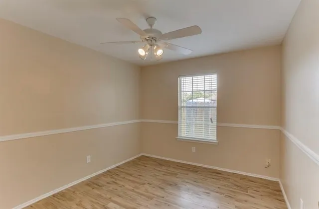 an empty room with wooden floor a ceiling fan a fireplace and windows