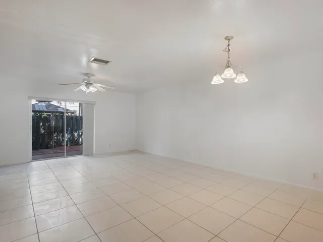 an empty room with chandelier fan and kitchen view