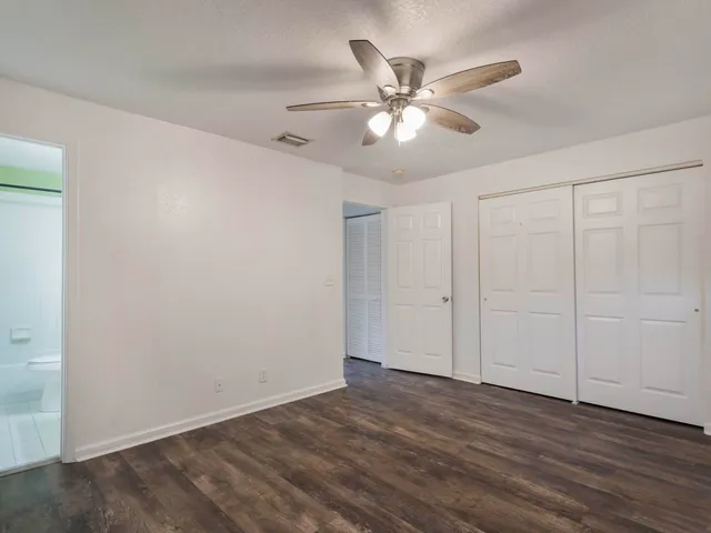 an empty room with wooden floor fan and windows