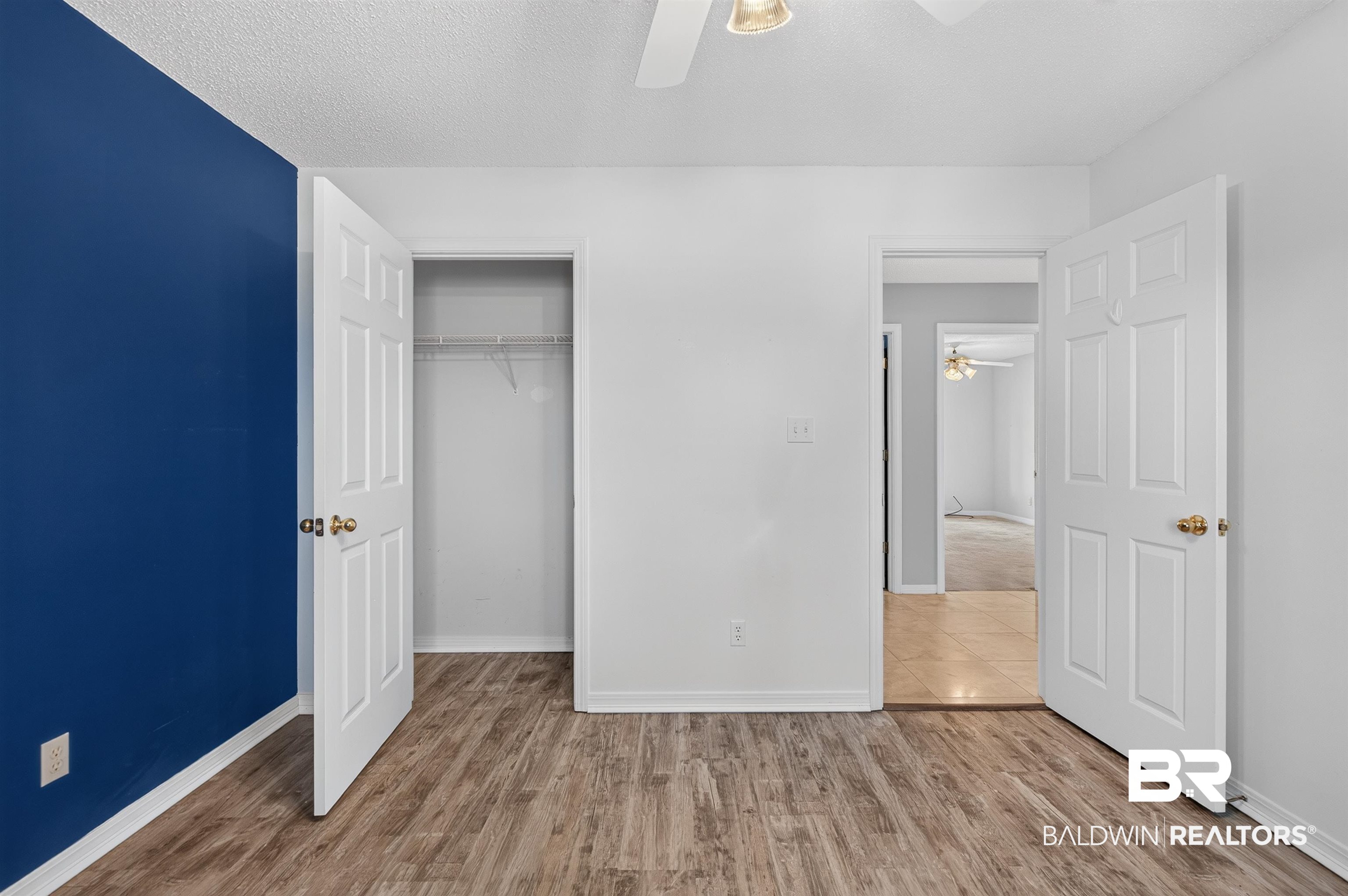 22685 County Road 12 Foley, AL 36535 - Photo 65 of 89 Room featuring wood-finish flooring, a contemporary blue accent wall, and a ceiling fan with integrated lighting