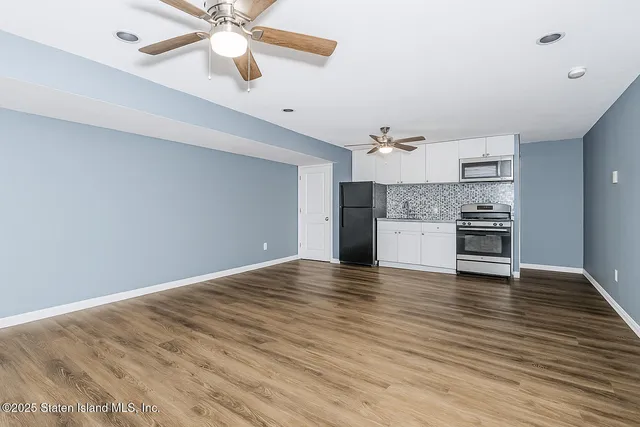 an empty room with wooden floor a ceiling fan and kitchen view