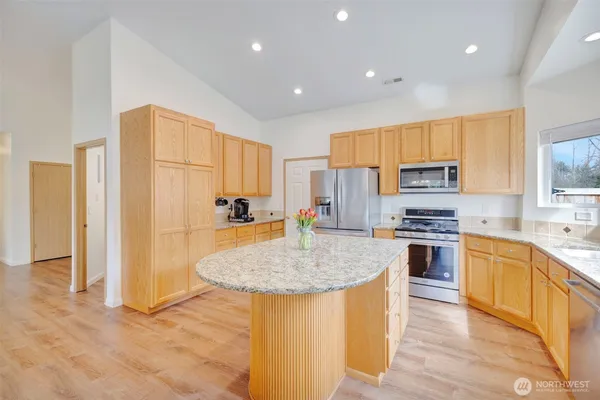 a kitchen with stainless steel appliances granite countertop a stove a sink a refrigerator and white cabinets with wooden floor