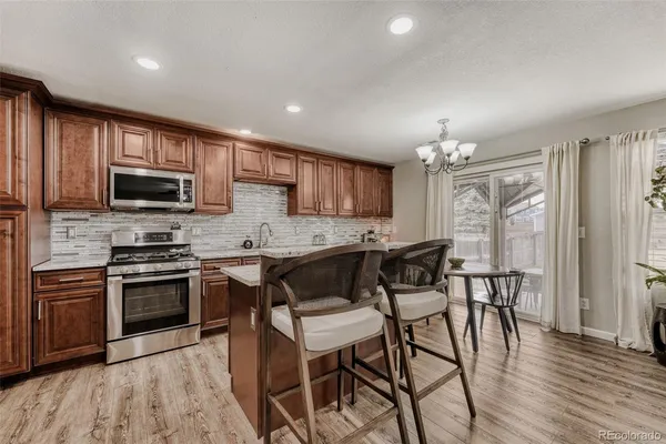 a kitchen with stainless steel appliances granite countertop a stove top oven a sink dishwasher a dining table and chairs with wooden floor