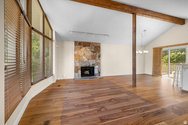 2088 Falcon Way Sandy, UT 84093 - Photo 5 of 46 Spacious living area featuring vaulted ceilings, exposed wood beams, a stone-clad fireplace, extensive wood-finish flooring, and large windows with integrated blinds