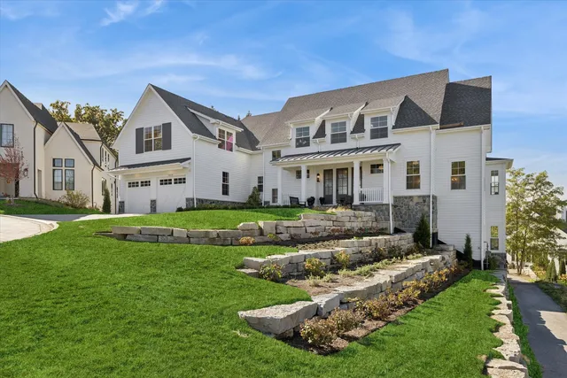a view of a white house in front of a big yard with plants and large trees