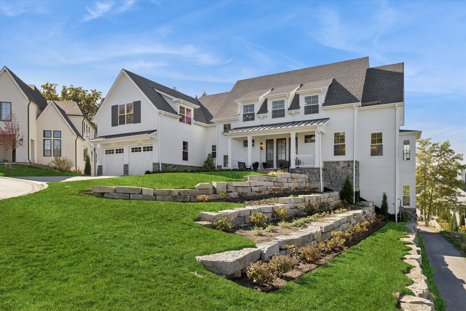 a view of a white house in front of a big yard with plants and large trees
