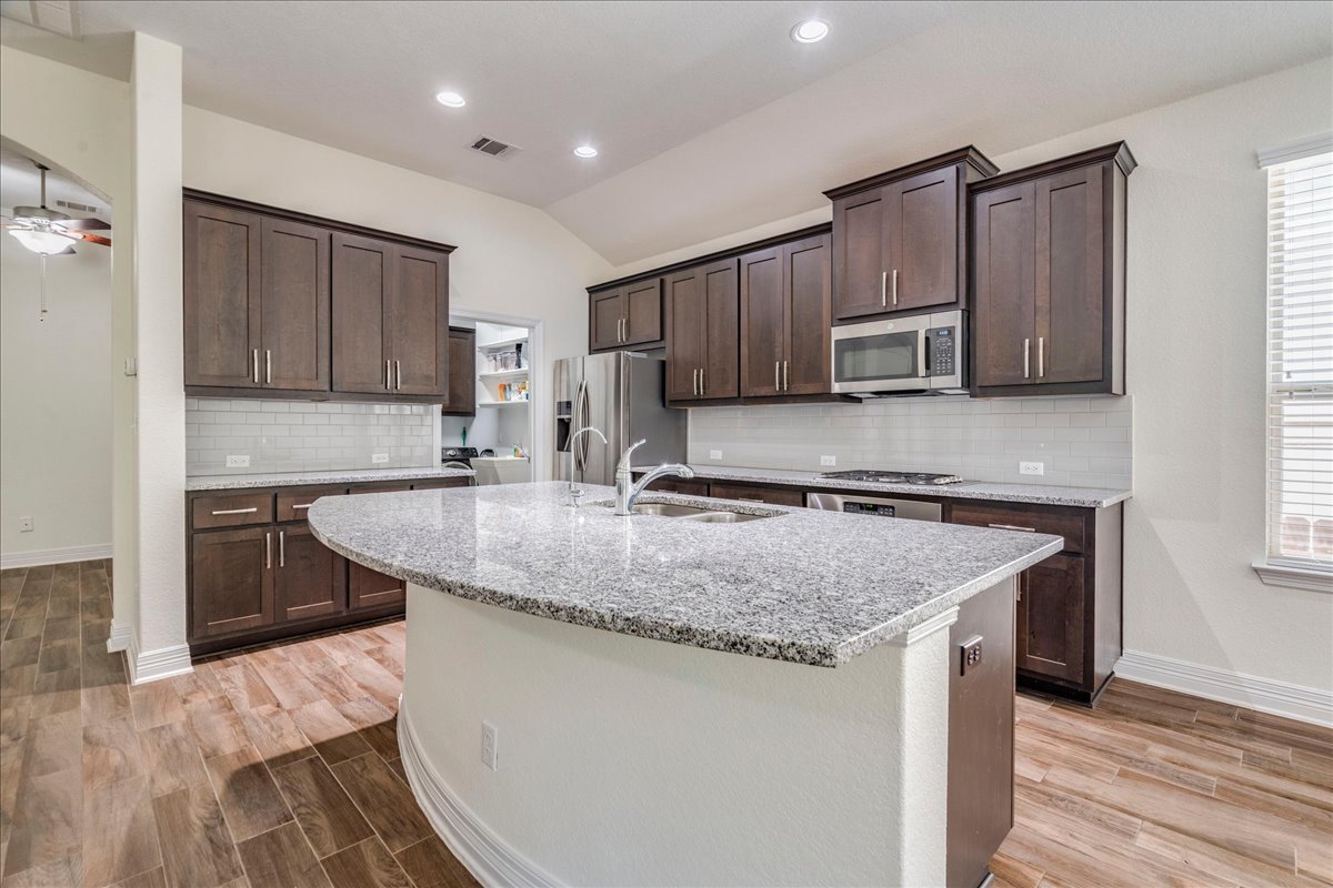 5009 Inks Clearing Lane Austin, TX 78738 - Photo 18 of 34 Rich dark wood cabinetry highlights this kitchen featuring a granite-topped curved island.