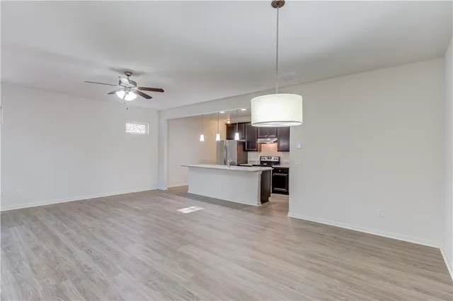 a view of an empty room and kitchen with wooden floor