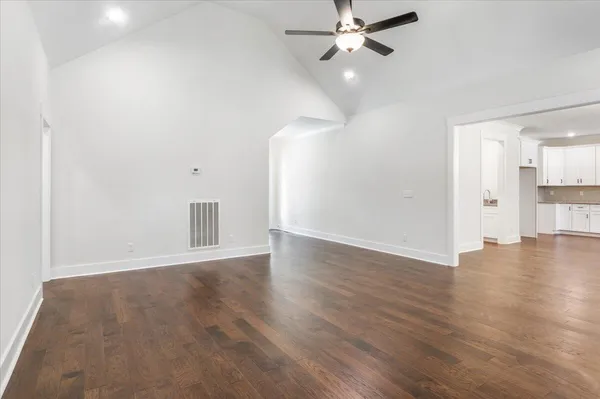 an empty room with wooden floor ceiling fan and windows
