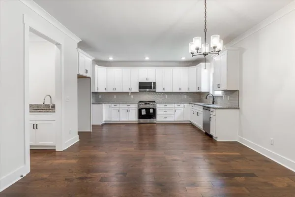 a open kitchen with stainless steel appliances granite countertop a sink a stove a refrigerator and white cabinets with wooden floor