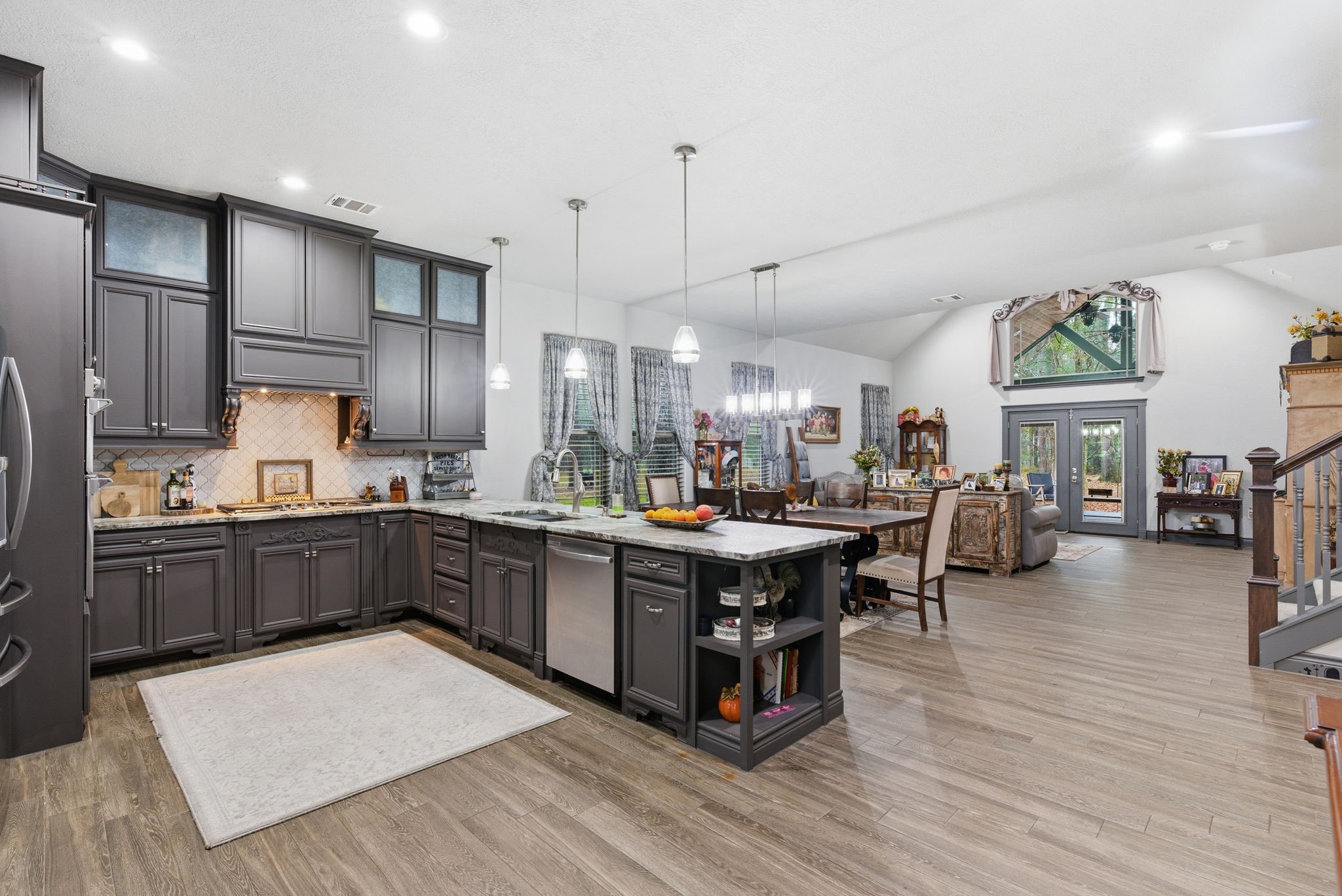 1480 Traylor Road Conroe, TX 77304 - Photo 6 of 25 Open-concept kitchen with large island, granite countertops, stainless steel appliances, and custom cabinetry. Vaulted ceilings and wood-look flooring flow seamlessly into the living and dining areas.”