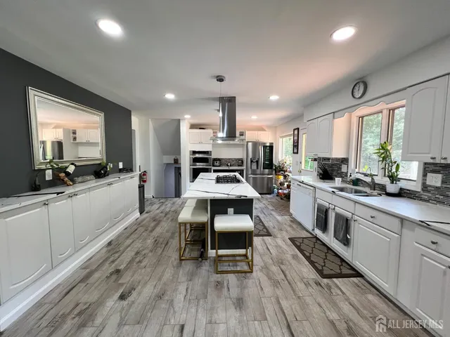 a large kitchen with stainless steel appliances granite countertop a stove a sink dishwasher a microwave oven and a dining table with wooden floor