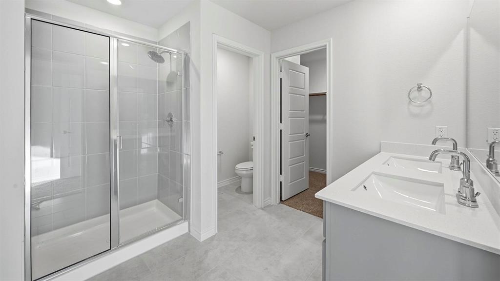 419 Epiphany Lane Lavon, TX 75166 - Photo 20 of 31 Bathroom featuring a dual vanity with undermount sinks, a frameless glass shower enclosure, a built-in shower bench, and light-toned tile flooring