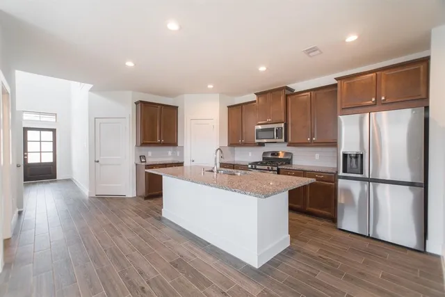 a kitchen with stainless steel appliances granite countertop a refrigerator a sink dishwasher a stove and white countertops with wooden floor