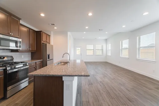 a kitchen with stainless steel appliances granite countertop a sink a stove a refrigerator cabinets and a wooden floor