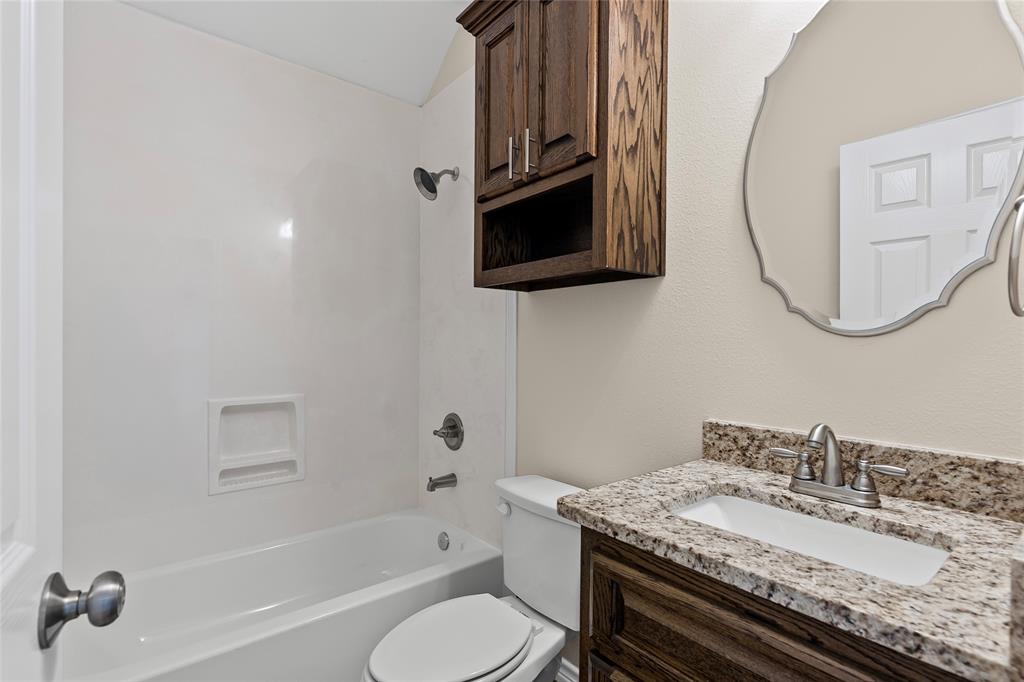 2910 Monroe Street Commerce, TX 75428 - Photo 25 of 34 a bathroom with a granite countertop sink a toilet and bathtub