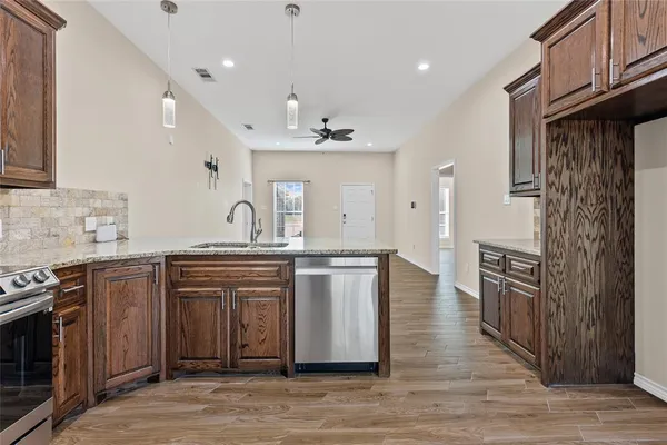 a large kitchen with stainless steel appliances granite countertop a stove a sink dishwasher and a refrigerator with wooden floor