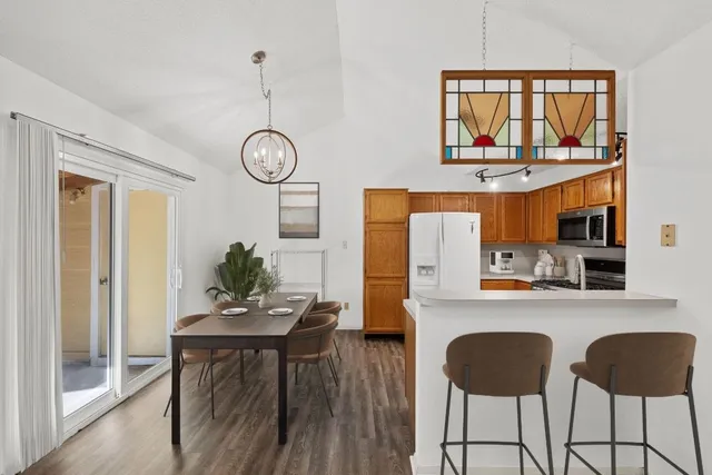 a kitchen with stainless steel appliances granite countertop a stove a refrigerator a microwave oven a dining table and chairs with wooden floor