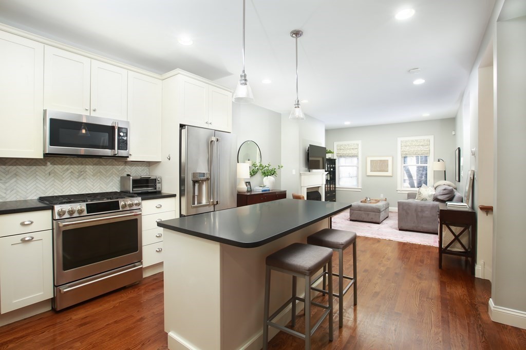 a kitchen with stainless steel appliances granite countertop a stove a refrigerator a kitchen island a sink a stove a dining table and chairs with wooden floor